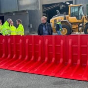 Håndværkere og gul gravemaskine bag rød Boxwall skybrudssikring
