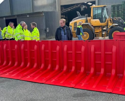 Håndværkere og gul gravemaskine bag rød Boxwall skybrudssikring