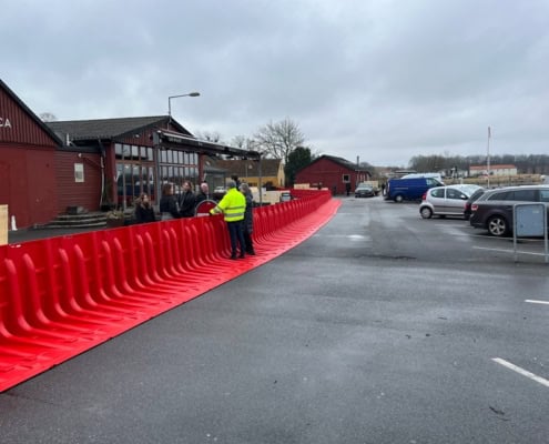 Lang række af Boxwall vandbarriere til bygning opstillet på våd asfalt